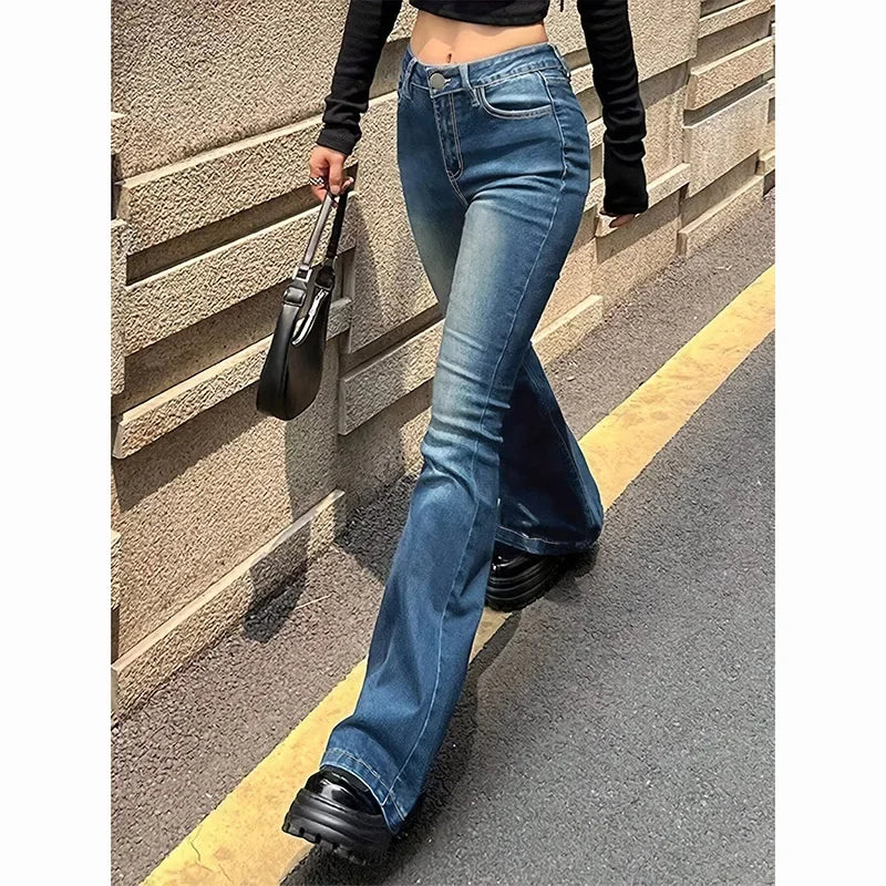 Person wearing blue flared jeans and black shoes against a textured wall. Women’s high waist flared jeans, stretchy bootcut denim trousers. Thin fabric, solid color, bell bottoms style for casual chic UK fashion.