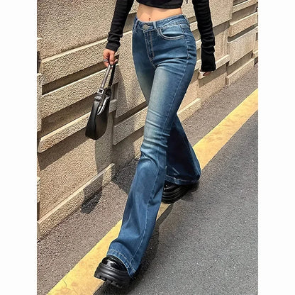 Person wearing blue flared jeans and black shoes against a textured wall. Women’s high waist flared jeans, stretchy bootcut denim trousers. Thin fabric, solid color, bell bottoms style for casual chic UK fashion.