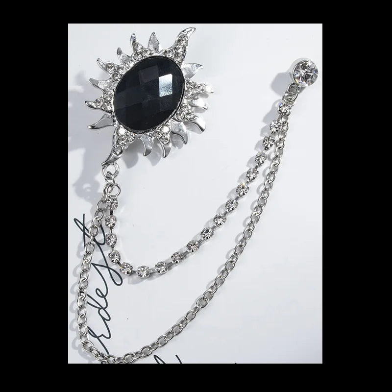 Decorative brooch with black central stone and silver chain on a white background. Elegant rhinestone lapel pins for men and women. Tassel, crown, floral pins for suits, collars, weddings, parties. Zinc alloy metal, classic style.