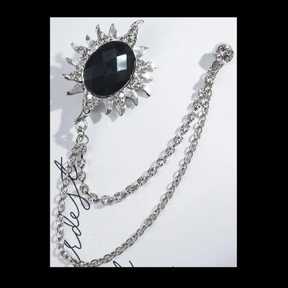 Decorative brooch with black central stone and silver chain on a white background. Elegant rhinestone lapel pins for men and women. Tassel, crown, floral pins for suits, collars, weddings, parties. Zinc alloy metal, classic style.