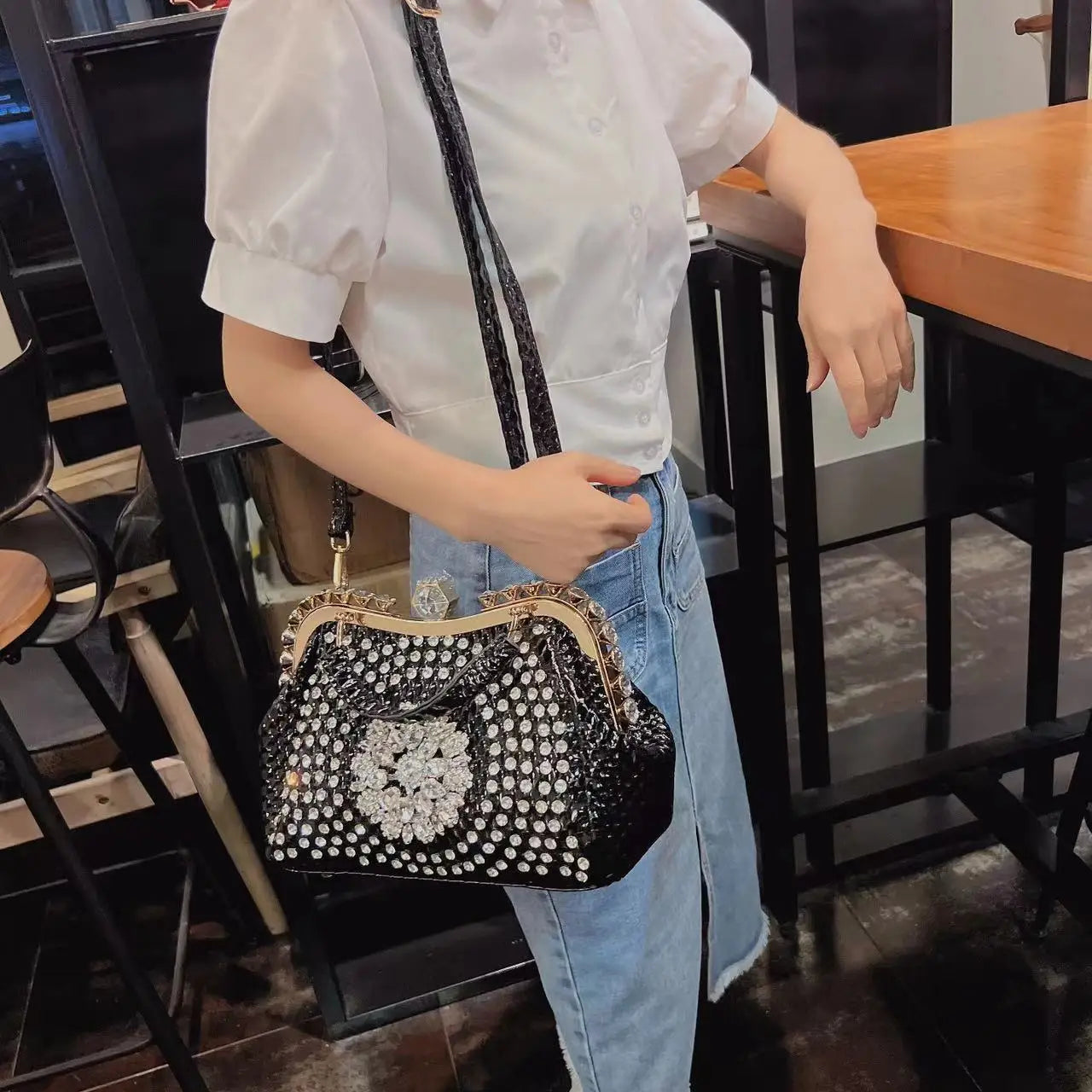 Person holding a black handbag with decorative elements in an indoor setting. Large genuine leather dumpling bag with diamond rhinestone clip and lock clasp. Soft handle, multiple compartments. Fashionable shoulder tote for women.