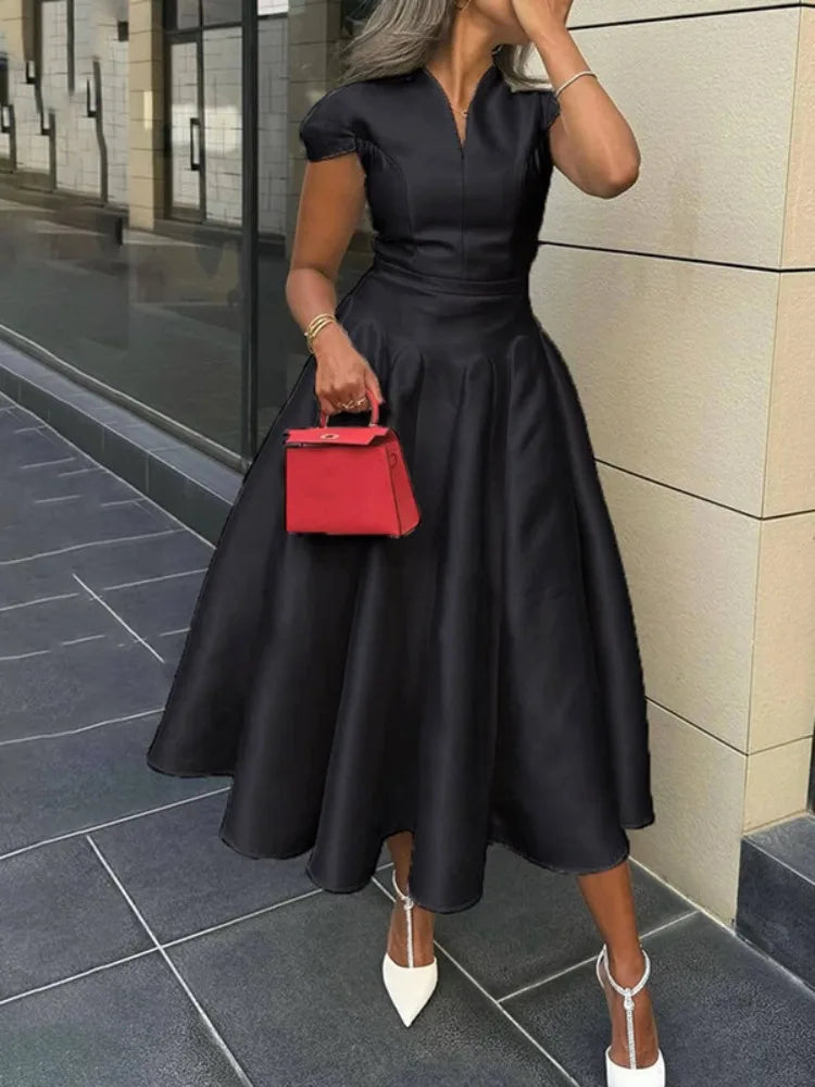 Woman in a black dress holding a red handbag on a city street.