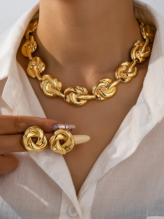 Woman wearing bold gold knot chain necklace and matching stud earrings with white shirt