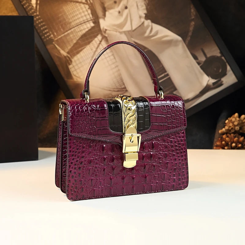 Purple crocodile-patterned handbag with gold clasp on a light surface, blurred vintage photo in the background. Small genuine leather crocodile crossbody bag. Hard flap design with soft handle, zipper closure, and interior phone & compartment pockets.