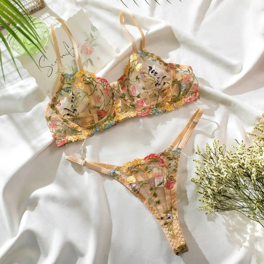 Floral embroidered lingerie set on a white fabric background with plants.