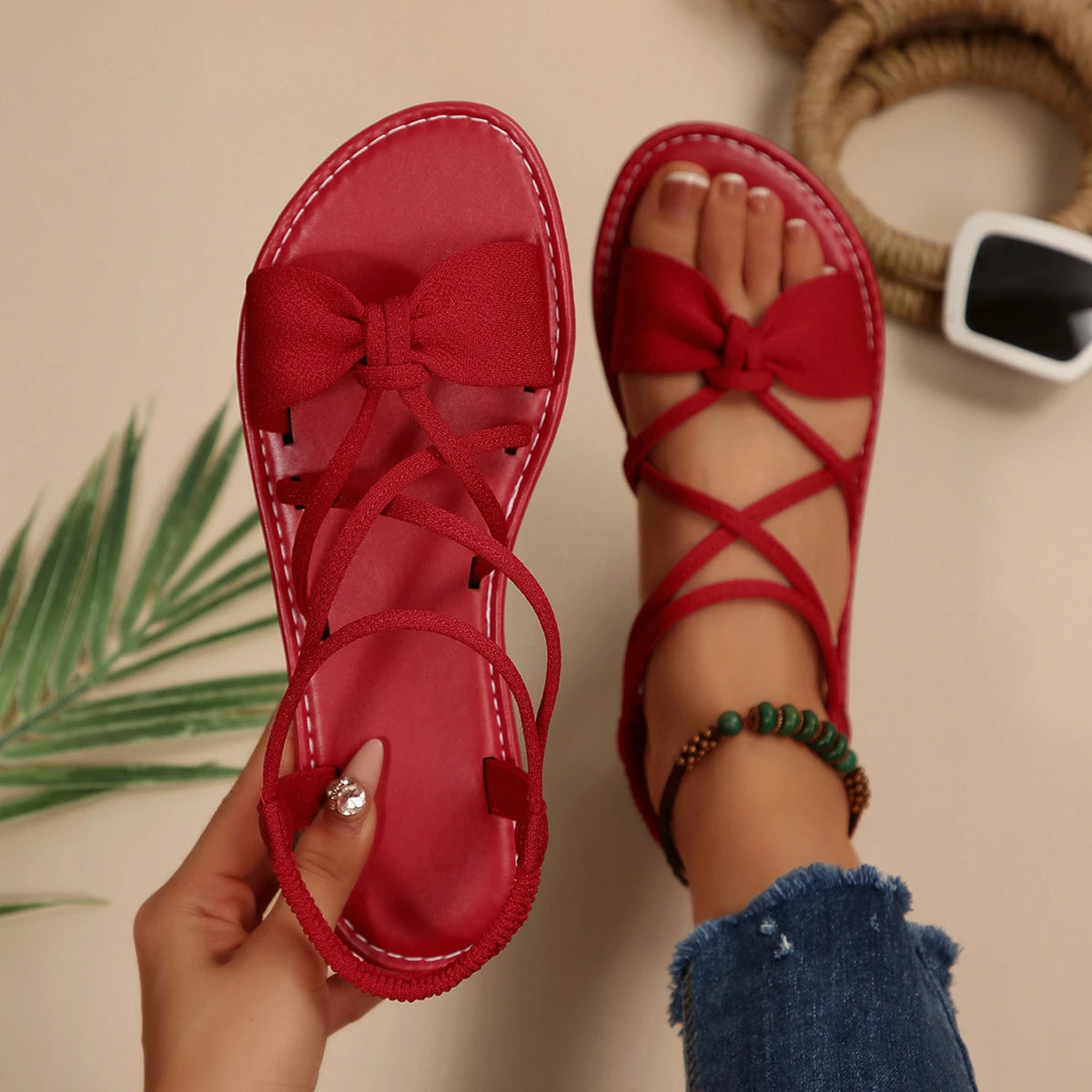 Red sandals with bow detail held by a hand on a neutral background