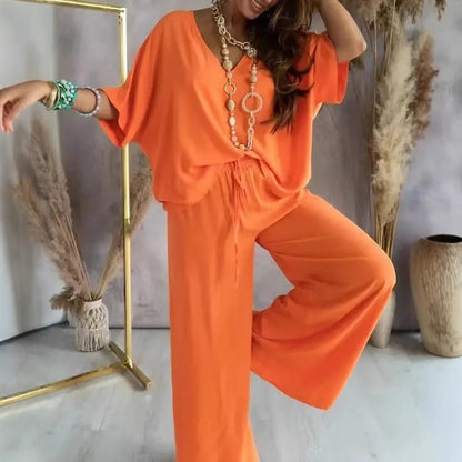 Person wearing an orange outfit with a gold necklace in a minimalistic setting.