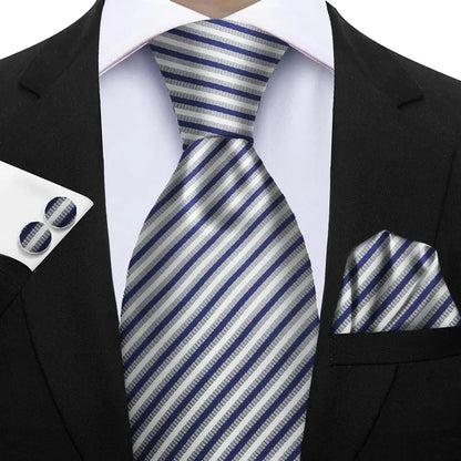 Black suit with a blue and gray striped tie, pocket square, and cufflinks. Elegant men’s 3-piece tie set: striped necktie, floral pocket square, matching cufflinks. Fashionable polyester accessories for formal occasions.