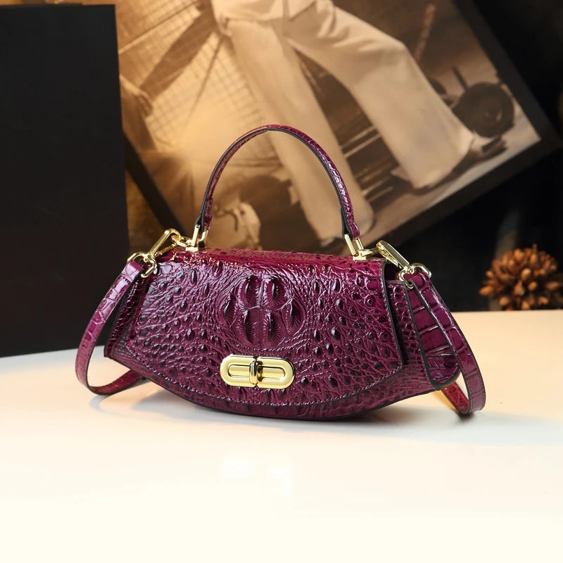 Purple crocodile-patterned handbag with gold accents on a light surface.