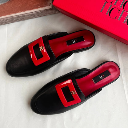 Black loafers with red buckles on a white surface, next to a red box.