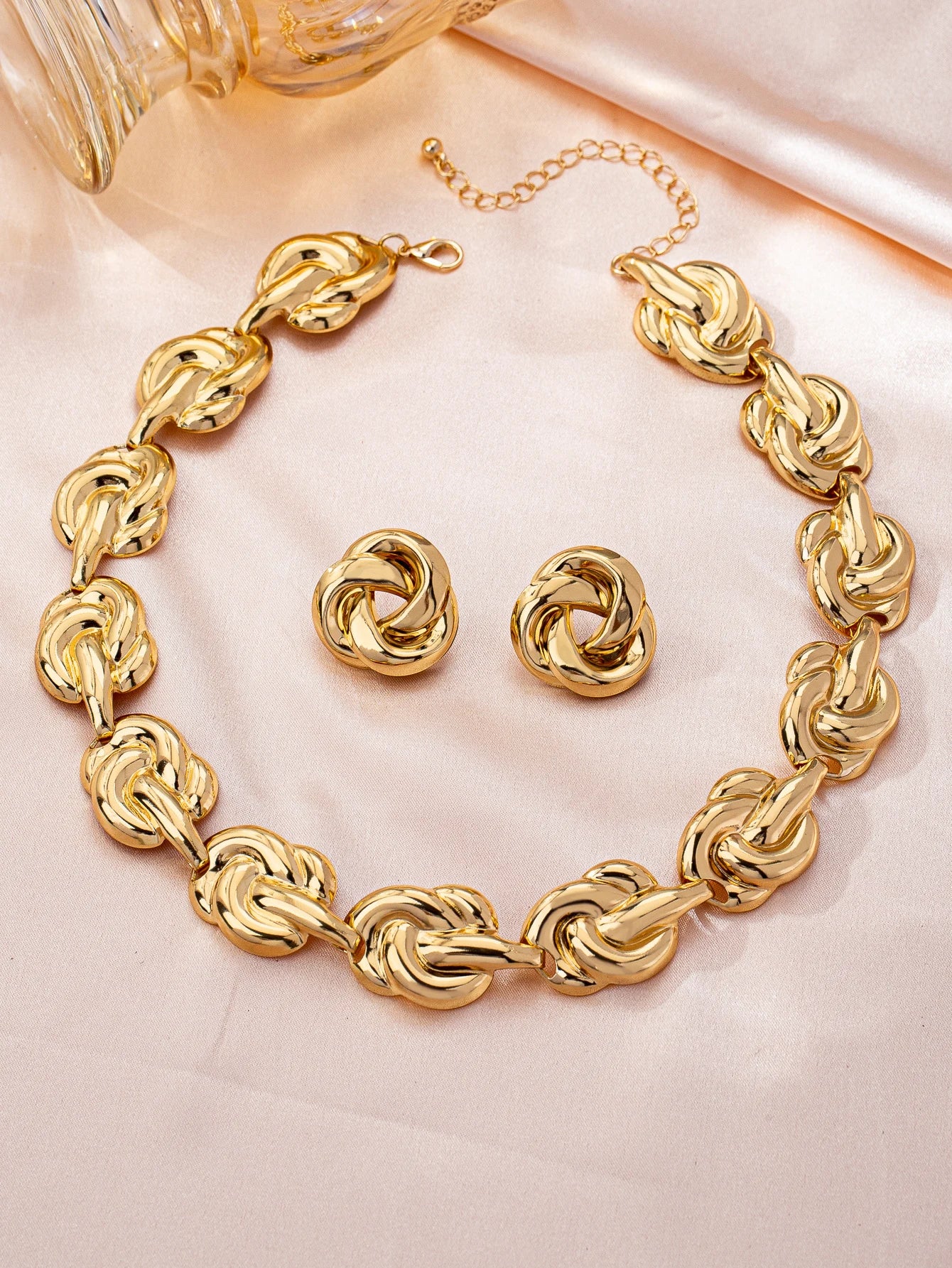 Gold knot chain necklace and matching stud earrings set on pink satin background