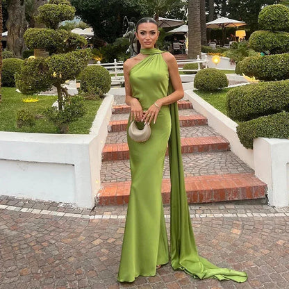 Woman in a green evening gown standing on a garden path with manicured hedges and trees.