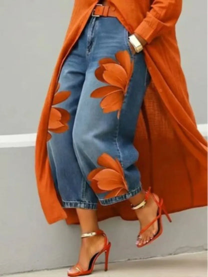 Person wearing an orange coat with floral patterns, blue jeans, and red high-heeled shoes against a gray background.