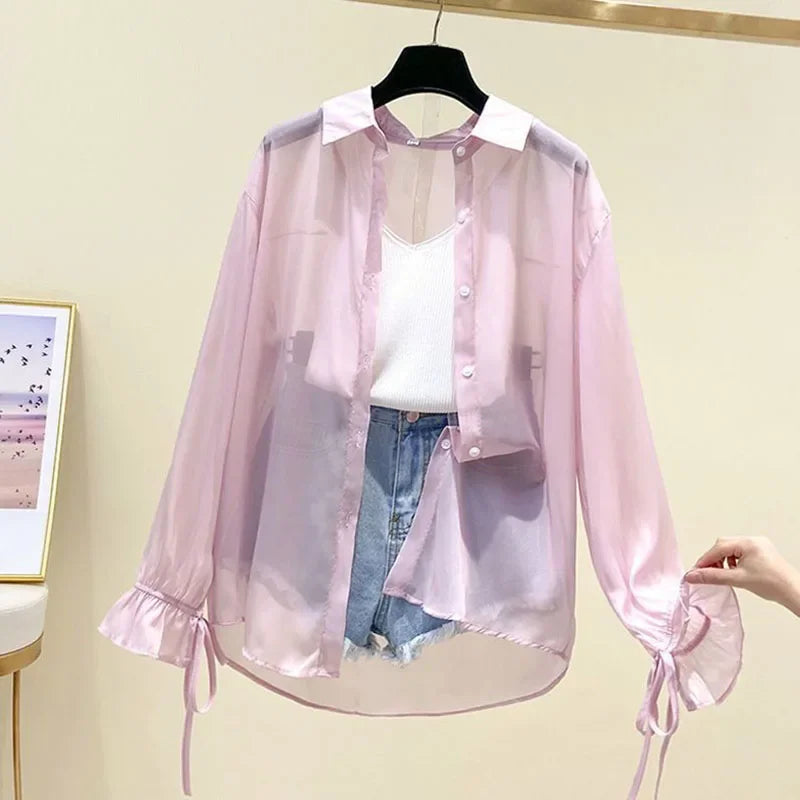 Pink sheer blouse with white top and blue jeans on a hanger against a beige wall.