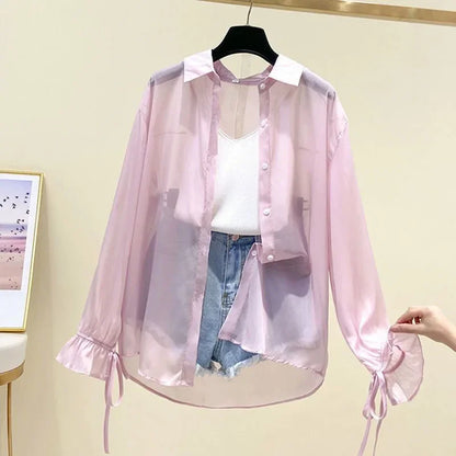 Pink sheer blouse with white top and blue jeans on a hanger against a beige wall.
