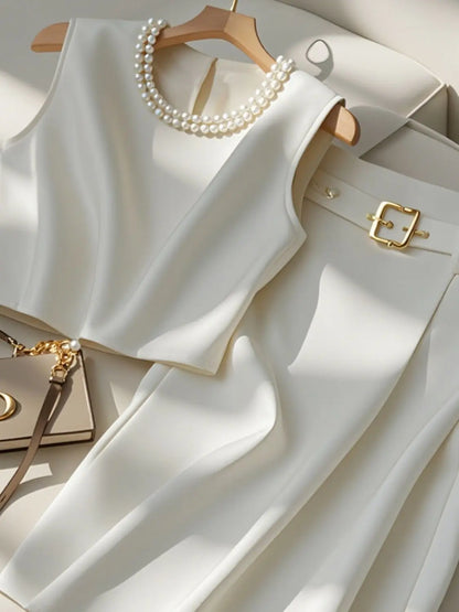 White sleeveless top with gold buckle, pearl necklace, and handbag on a light background. Women’s high-end two-piece set with sleeveless O-neck crop top and mid-calf A-line skirt. Elegant, minimalist office suit, beaded detail, UK fashion.