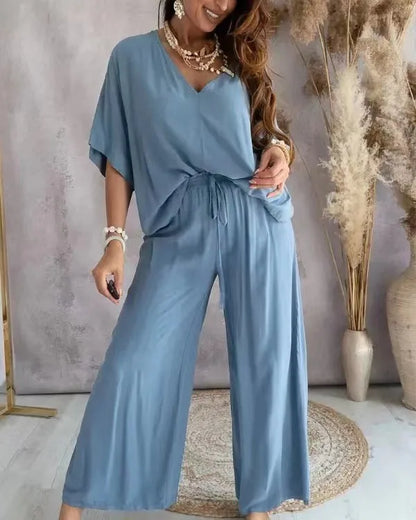Woman wearing a blue jumpsuit standing in a room with decorative elements.
