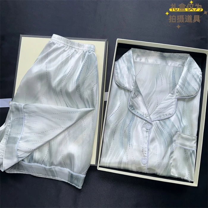 White satin shirt and pants set in open boxes on a dark background. Women’s cherries print summer pajamas set—faux satin V-neck top and shorts, funny cute style. Lightweight, comfortable, UK fashion set.