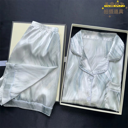 White satin shirt and pants set in open boxes on a dark background. Women’s cherries print summer pajamas set—faux satin V-neck top and shorts, funny cute style. Lightweight, comfortable, UK fashion set.