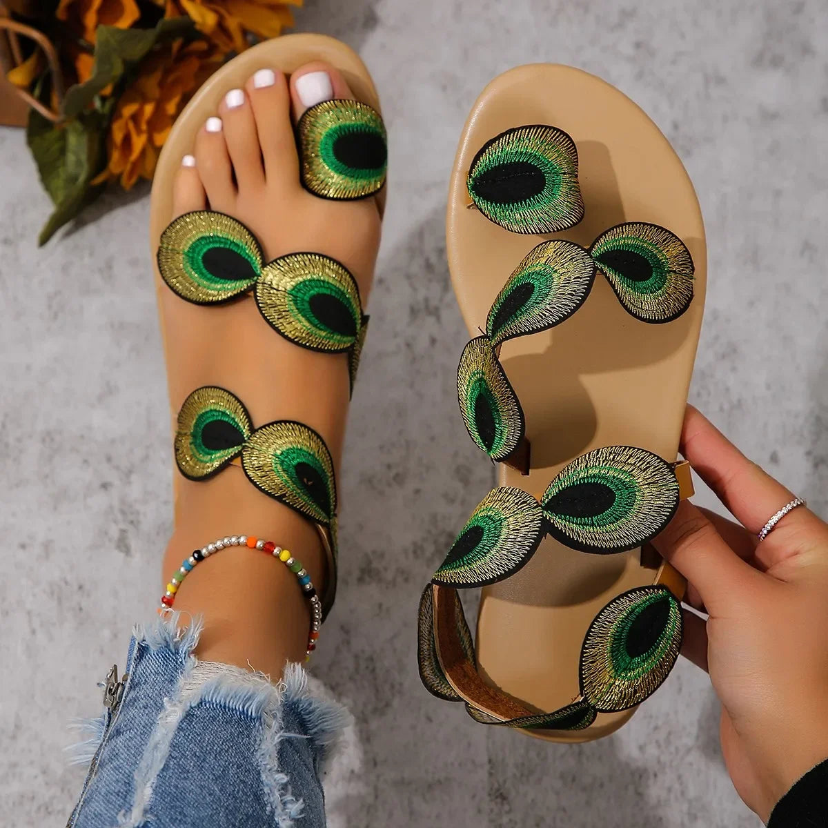 Beige sandals with peacock feather designs on a gray surface