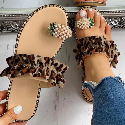 Beige sandals with leopard print ruffles and pearl embellishments worn by a person.