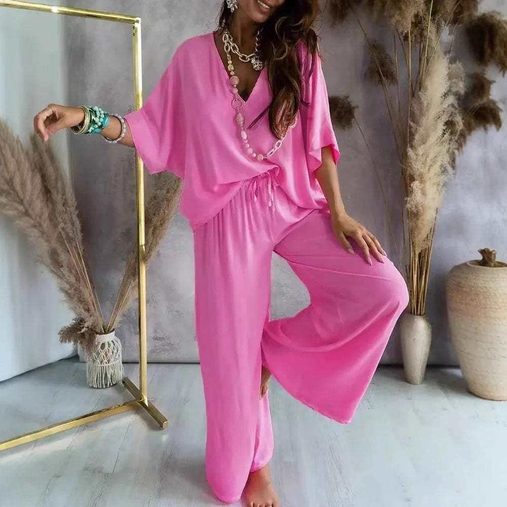 Woman in a pink outfit posing in a room with decorative plants and a mirror.