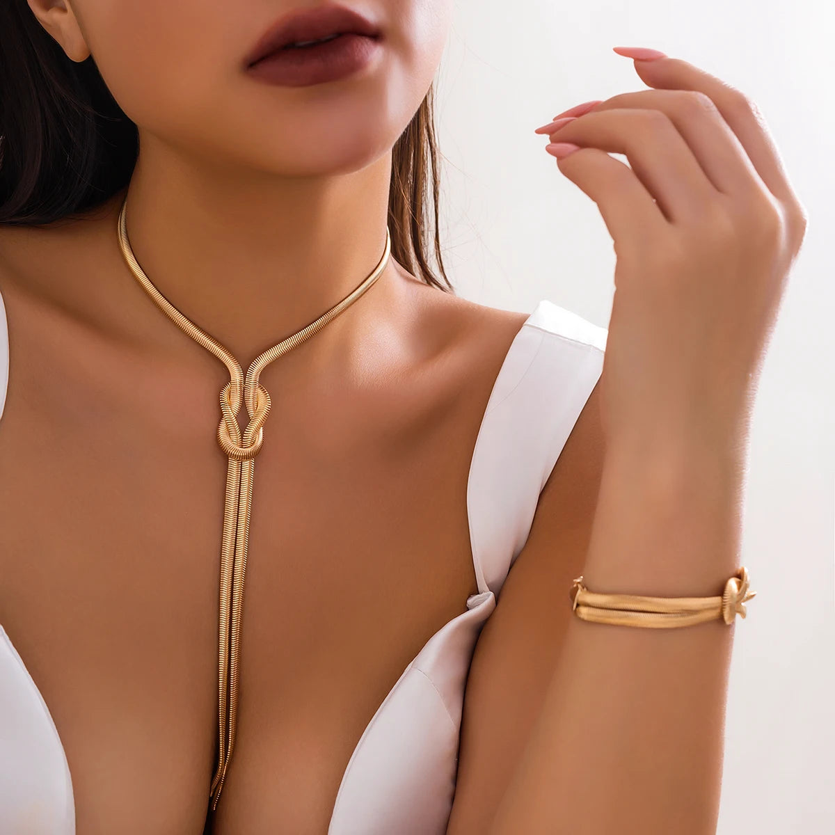 Close-up of a person wearing a gold necklace and bracelet on a plain background. Women’s vintage goth snake twisted chain necklace & bracelet set with tassel, Y2K style jewelry accessories for fashion-forward looks.