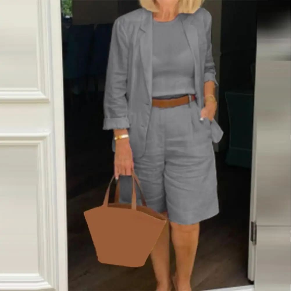 Image of a woman wearing a white Linen Look Blazer and Bermuda Shorts Co-ord Set with a brown belt and straw bag. Ideal smart casual summer outfit.