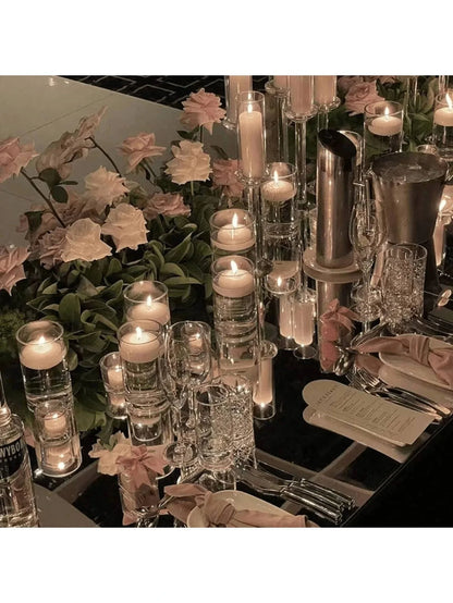 Elegant table setting with candles, glasses, and flowers on a reflective surface.
