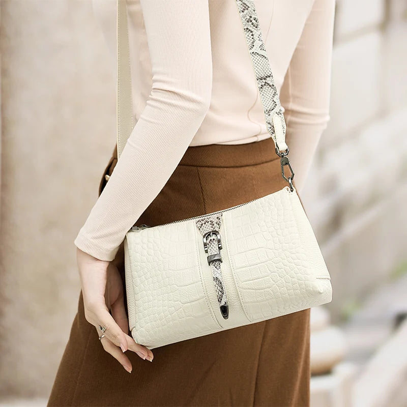 White handbag with snake detail held by a person wearing a beige top and brown skirt. Genuine leather women’s shoulder messenger bag in black and gray. Soft cow leather, flap style with zipper closure. Perfect versatile bag for all seasons.