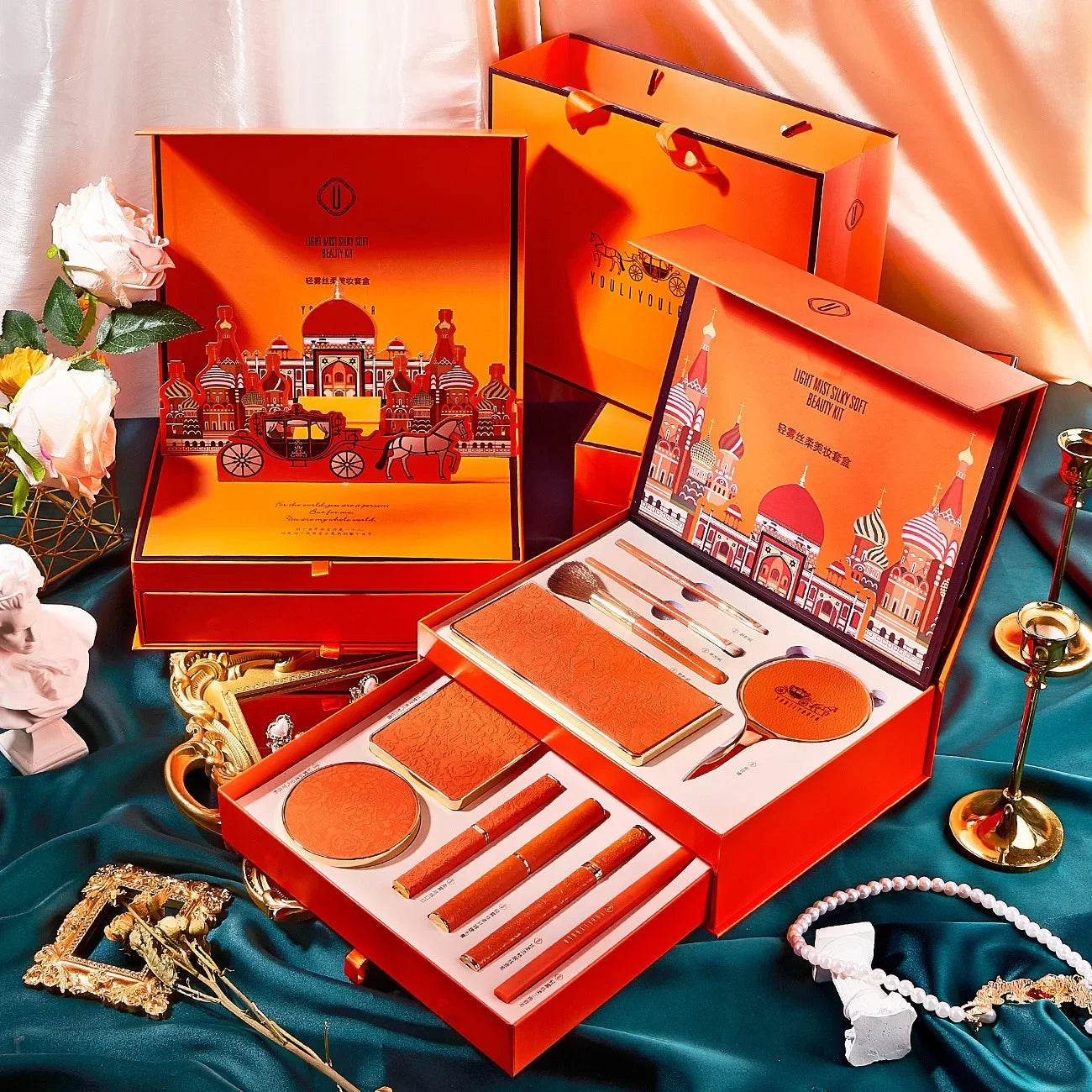 Orange cosmetic set with decorative packaging on a blue fabric background. Christmas makeup gift box with BB cream, lipstick, eyeshadow, eyebrow pencil, and brushes. Holiday beauty set for women & girls.