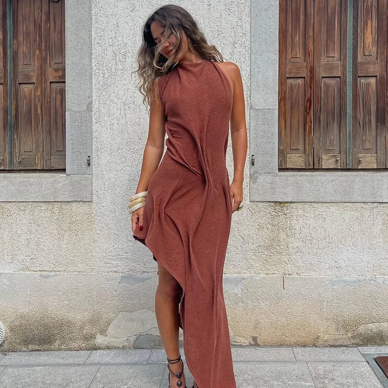 Woman wearing a rust-colored dress standing against a stone wall.
