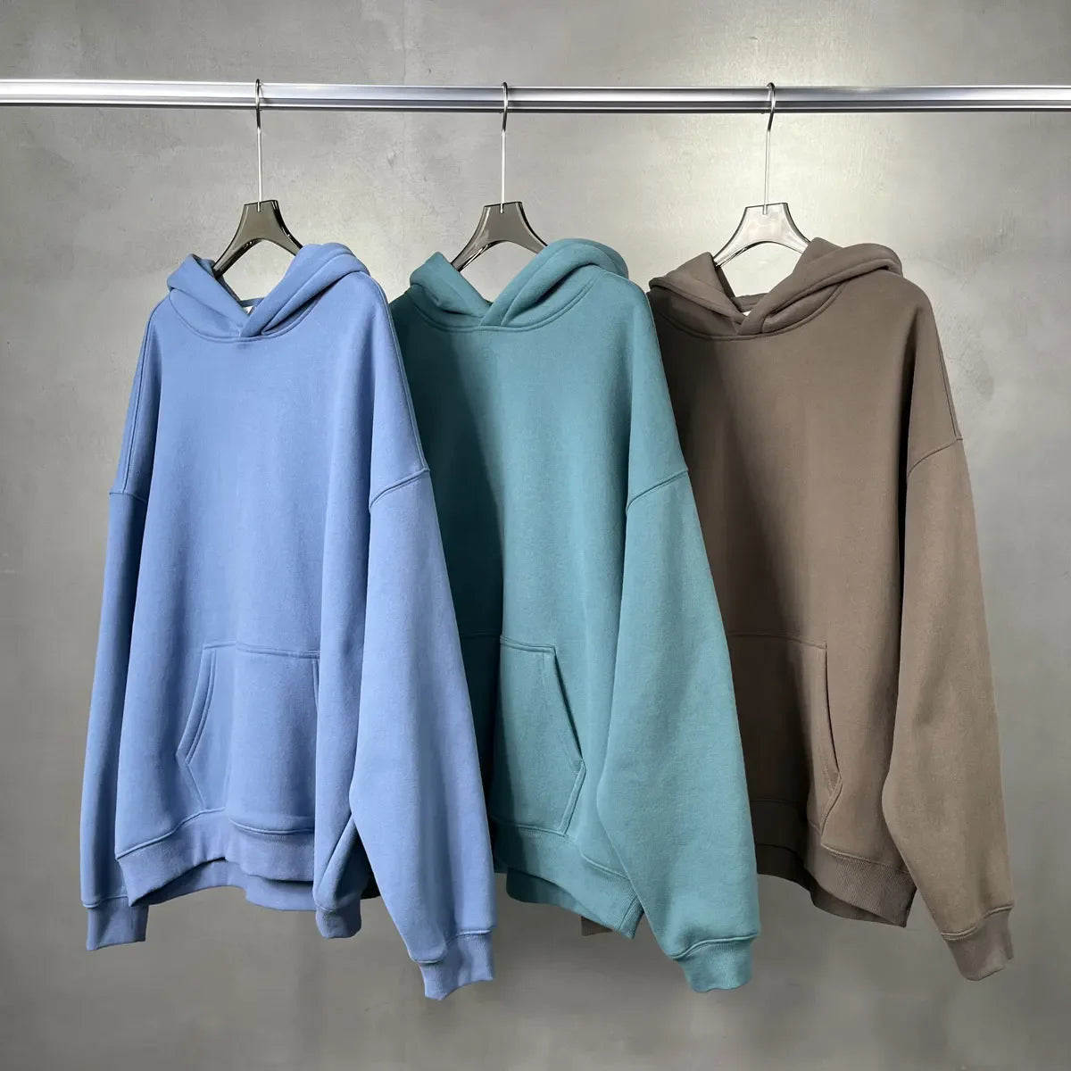 Three hoodies in blue, green, and brown hanging on a rack against a gray background