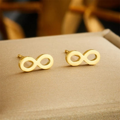 Gold infinity symbol earrings on a beige surface
