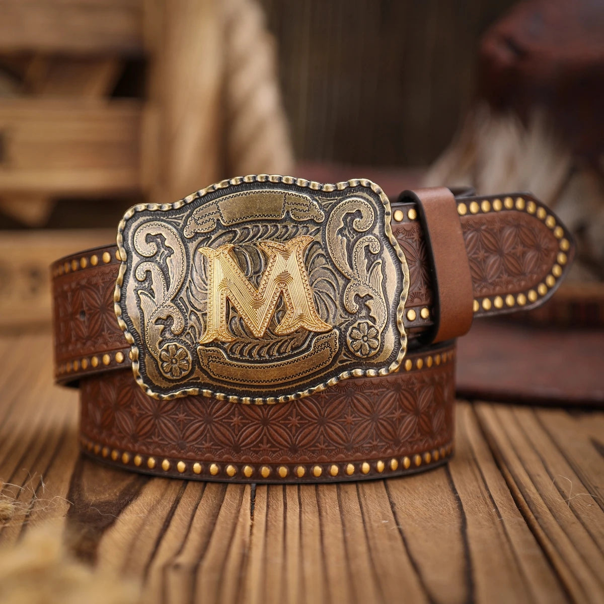 Brown leather belt with gold 'M' buckle on a wooden surface