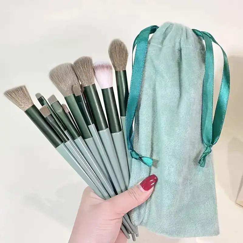 Set of makeup brushes with green handles held by a hand, next to a green drawstring bag on a white background. Soft fluffy makeup brush set with wool fiber bristles and plastic handles. Complete set for powder, foundation, eyeshadow, and beauty blending.