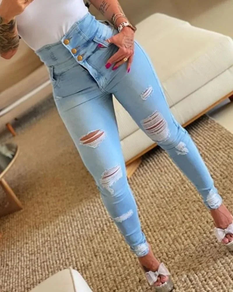 Person wearing light blue distressed jeans indoors. Women’s slim pencil jeans, high waist bodycon fit. Casual sheath denim trousers with button detail, ankle length. Trendy Y2K style UK.