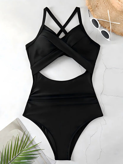 Black swimsuit with cut-out design on a light surface with sunglasses and a leaf.