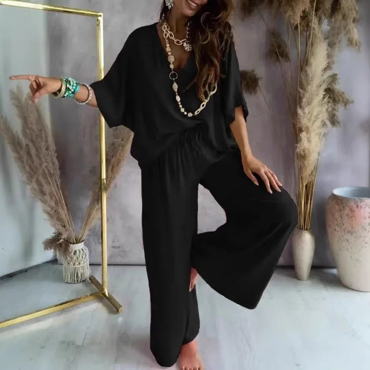 Woman in a black outfit posing in a room with decorative plants and a mirror.