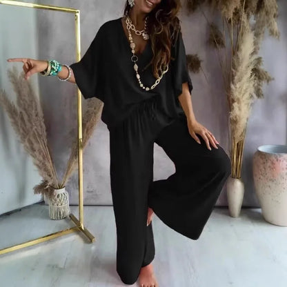Woman in a black outfit posing in a room with decorative plants and a mirror.