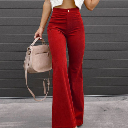 Person wearing red pants holding a beige handbag against a gray wall. Slim micro flare corduroy trousers with elastic waistband, screw thread button detail, casual style for women. Available in multiple colors UK FTF Market.