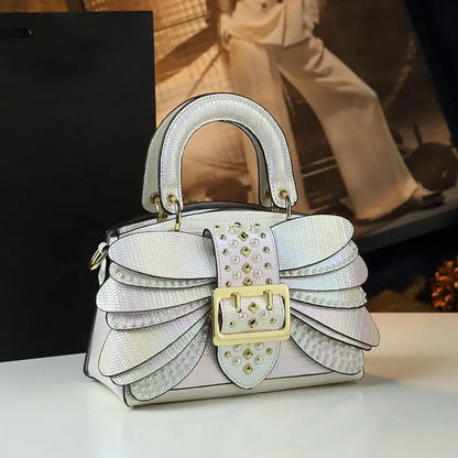 White handbag with gold accents on a white surface. Women’s pearl riveted leather bag—animal print, trapezoid box shape, shoulder/crossbody style, soft handle, stylish UK fashion messenger handbag.