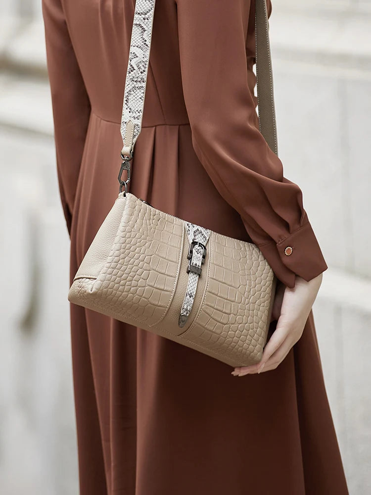 Person holding a beige handbag with a snake print strap against a neutral background. Genuine leather women’s shoulder messenger bag in black and gray. Soft cow leather, flap style with zipper closure. Perfect versatile bag for all seasons.