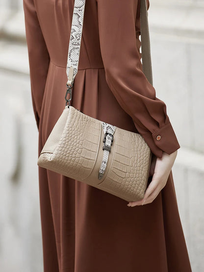 Person holding a beige handbag with a snake print strap against a neutral background. Genuine leather women’s shoulder messenger bag in black and gray. Soft cow leather, flap style with zipper closure. Perfect versatile bag for all seasons.