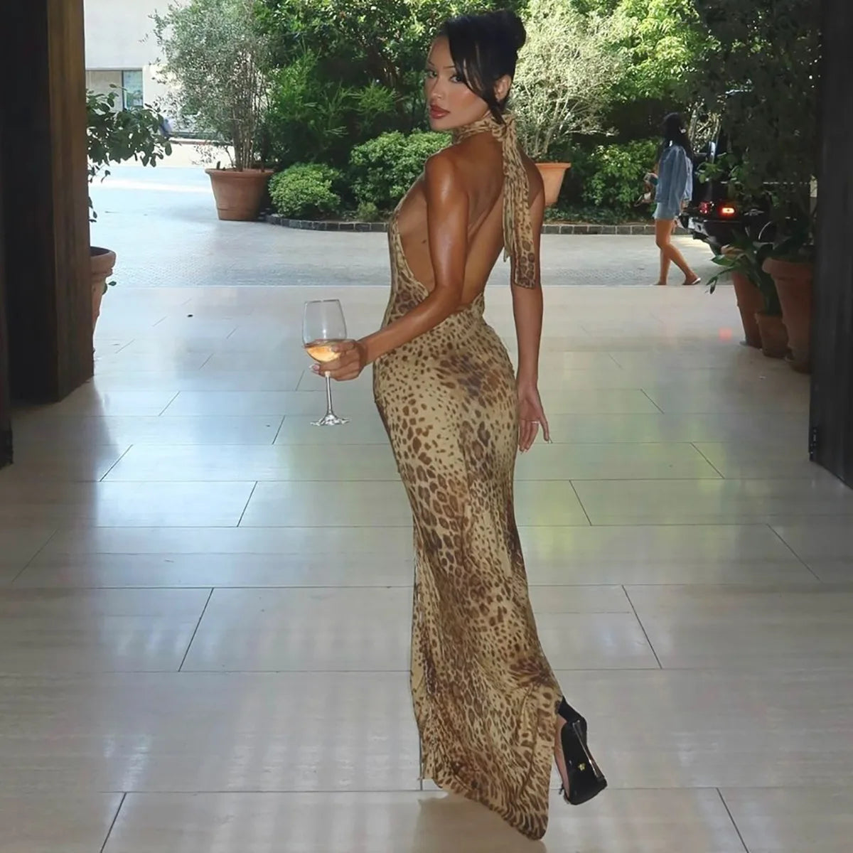 Woman in a leopard print dress holding a glass of wine on a patio.