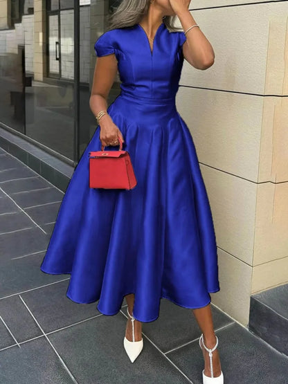 Woman in a blue dress holding a red handbag on a city street.