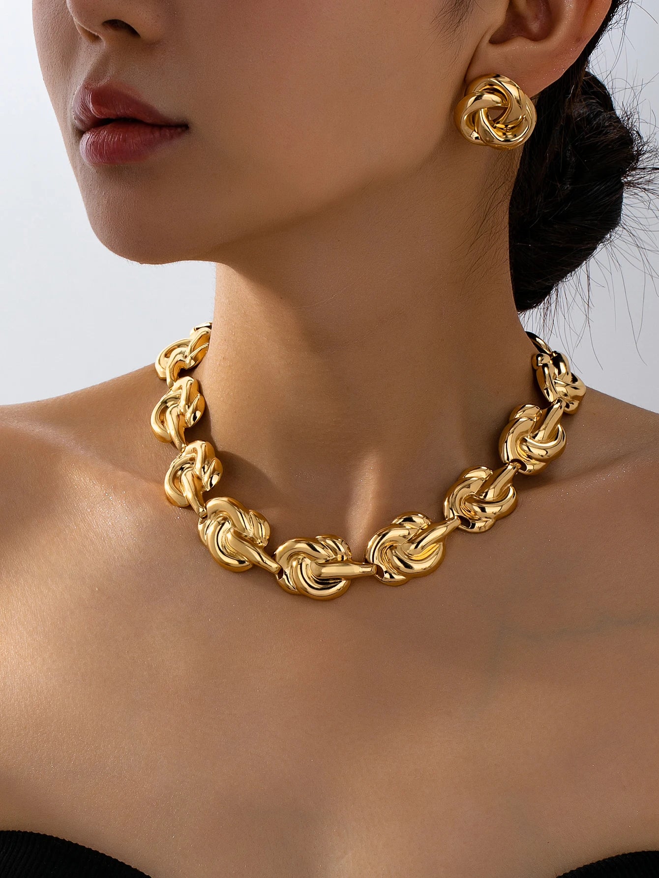 Close-up of woman wearing gold chunky knot chain necklace and geometric stud earrings