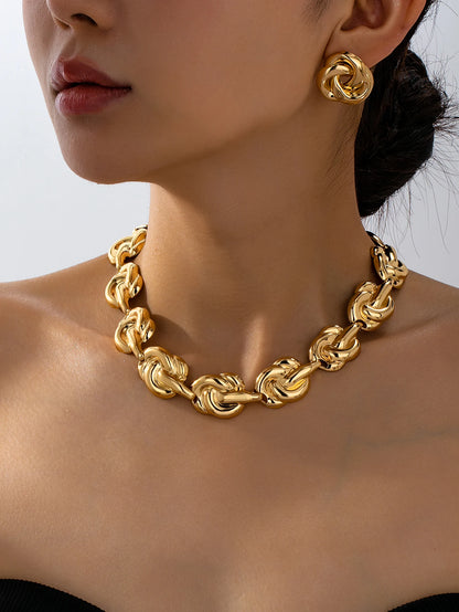 Close-up of woman wearing gold chunky knot chain necklace and geometric stud earrings