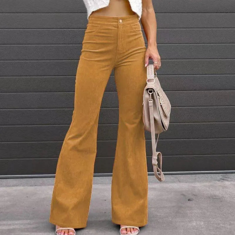 Person wearing mustard yellow flared pants against a gray wall. Slim micro flare corduroy trousers with elastic waistband, screw thread button detail, casual style for women. Available in multiple colors UK FTF Market.