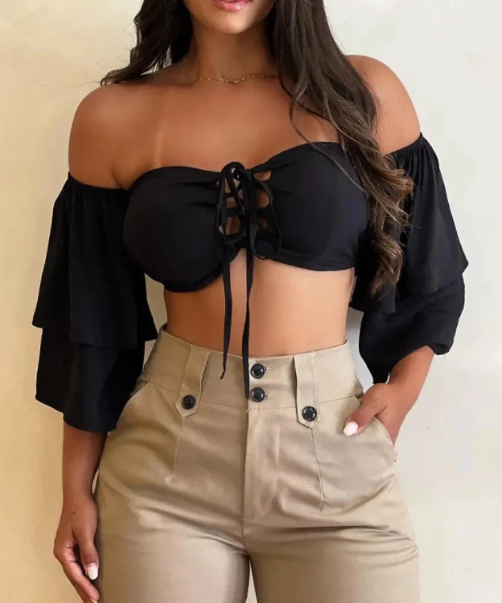 Woman wearing a black off-shoulder top and beige pants against a neutral background